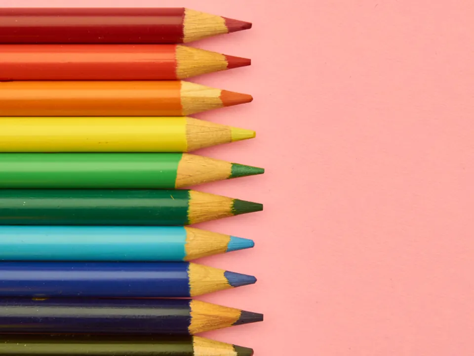 Rainbow row of colored pencils on a pink background