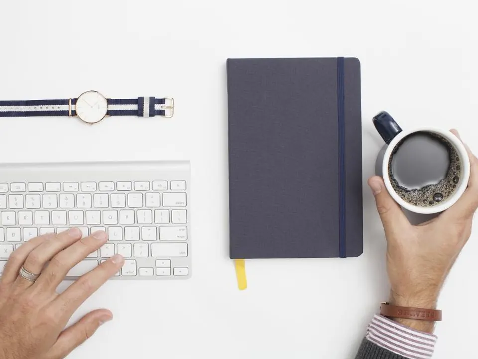Minimal desk with a notebook, keyboard and a cup of coffee