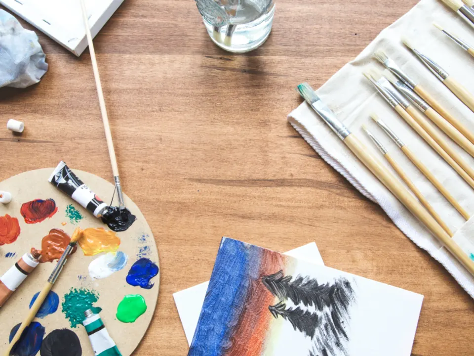 Artist's palette, paint tubes and brushes on a wooden studio table