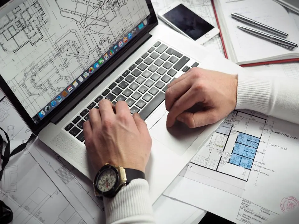 Designer working on a laptop beside printed layout sketches