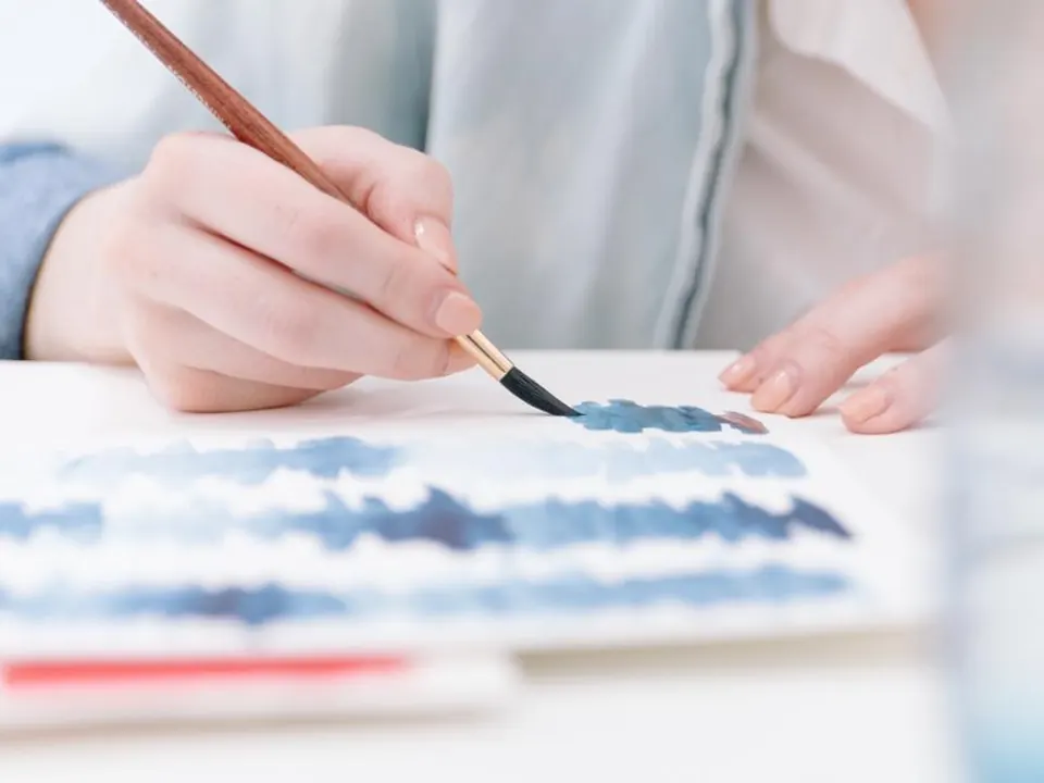 An illustrator painting a watercolor wash with a fine brush