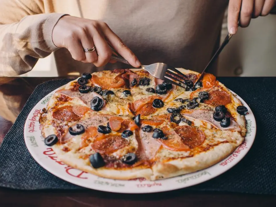 Hands slicing a pepperoni and olive pizza